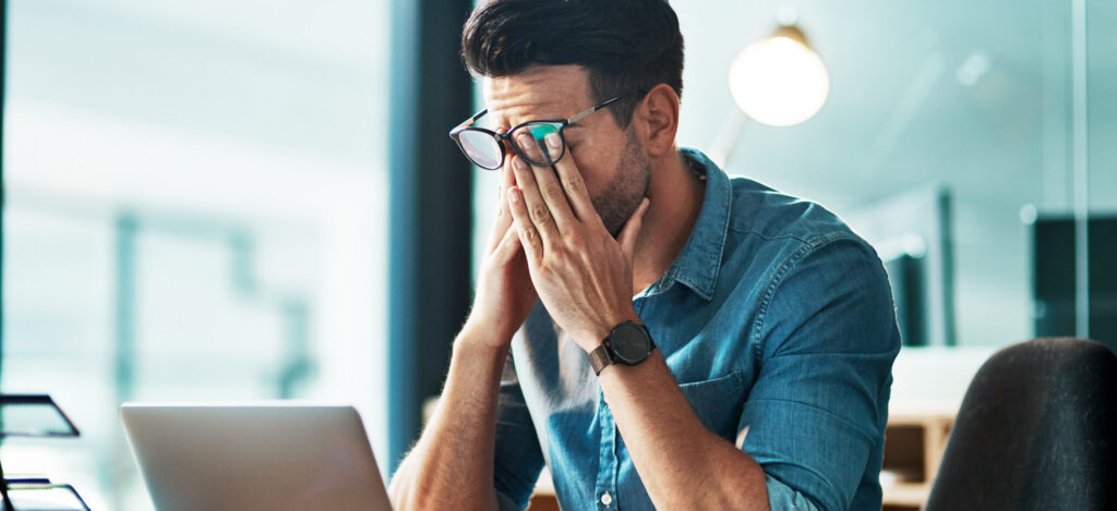 Mann sitzt am PC und reibt sich die Augen: Trotz viel Schlaf ist er ständig müde, was auf einen Vitamin-12-Mangel hindeuten kann.