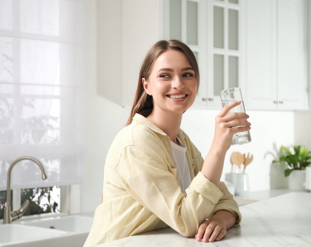 Frau mit einem Glas Wasser in der Küche: Sie nimmt Vitamin B12 ein und fragt sich, ob eine Überdosierung möglich ist.