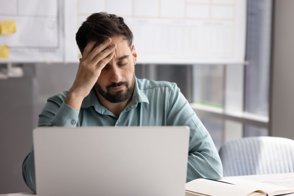 Mann sitzt vor seinem Laptop, die Hand auf der Stirn.